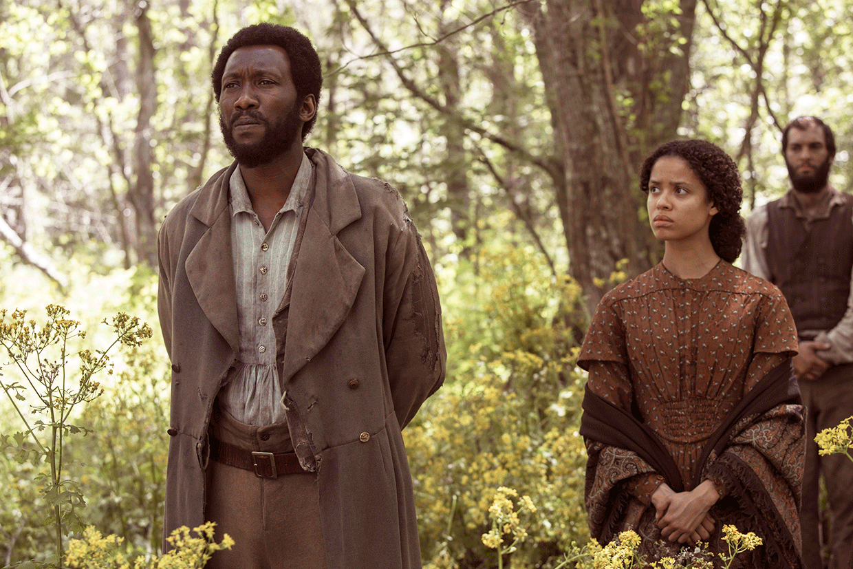 Moses (Mahershala Ali) and Rachel (Gugu Mbatha-Raw) listen as Newt addresses his men about race. © 2015 STX Productions.