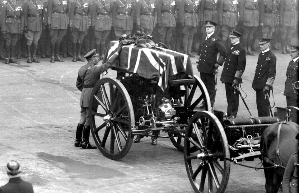 The coffin of the Unknown Warrior on a coach covered with a Union flag. King George V and soldiers accompany it.