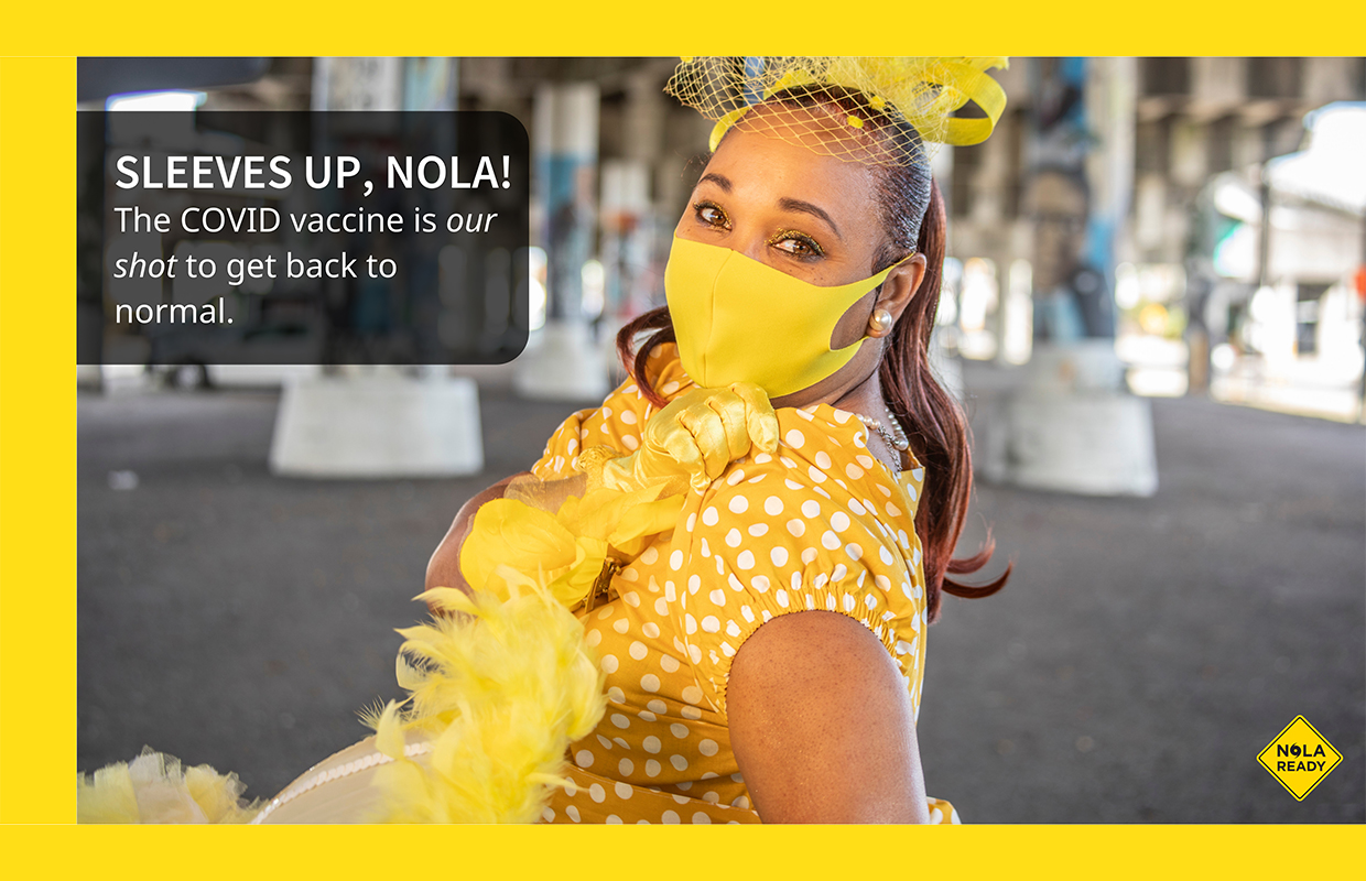 A Poster of a woman in a yellow Mardi Gras costume and mask and the slogans Sleeves Up, NOLA and the COVID vaccine is our shot to get back to normal.