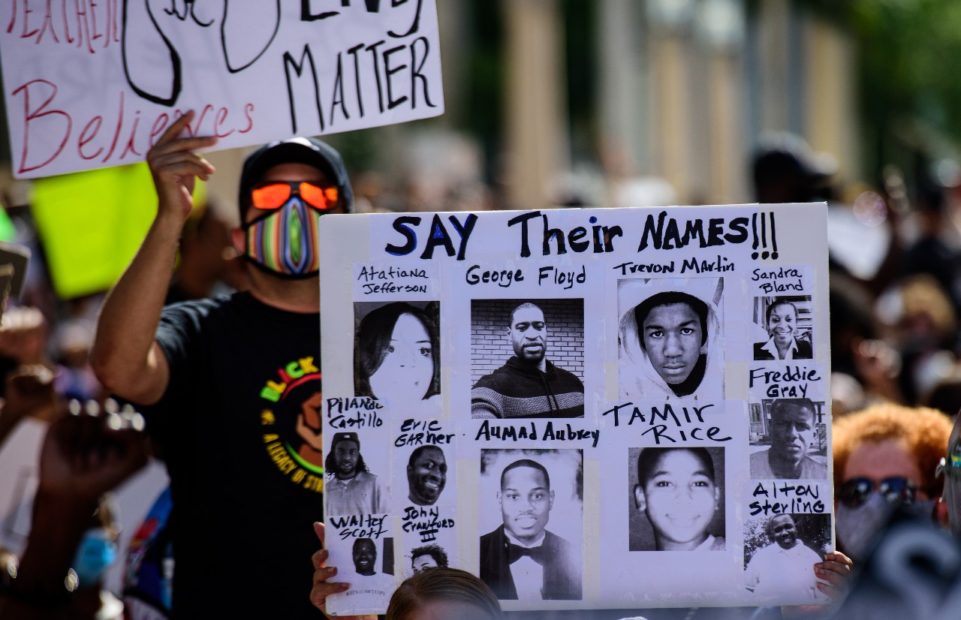 A protester holding a homemade sign with the slogan "Say Their Names": George Floyd, Tamir Rice, Atatiana Jefferson, Trayvon Martin, Ahmed Aubrey, Eric Garner, Sandra Bland, Freddie Gray, Alton Sterling