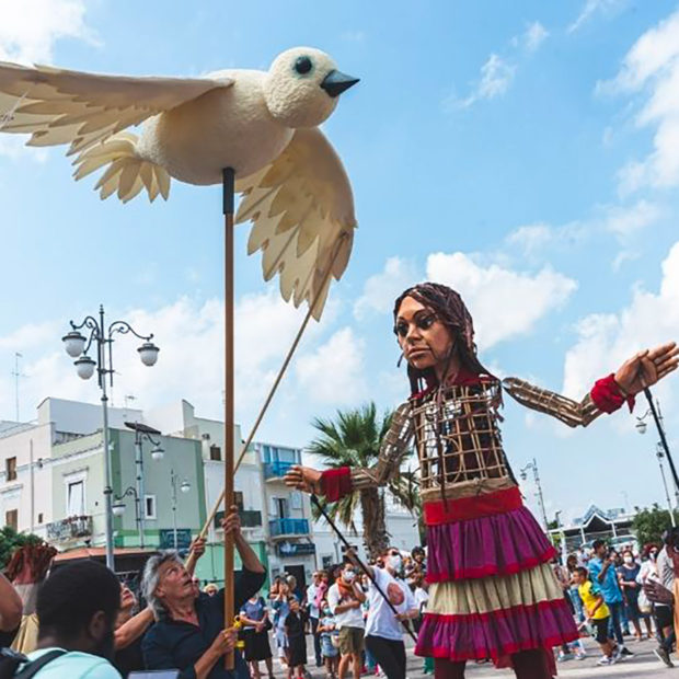 Little Amal interacting with a white dove puppet.