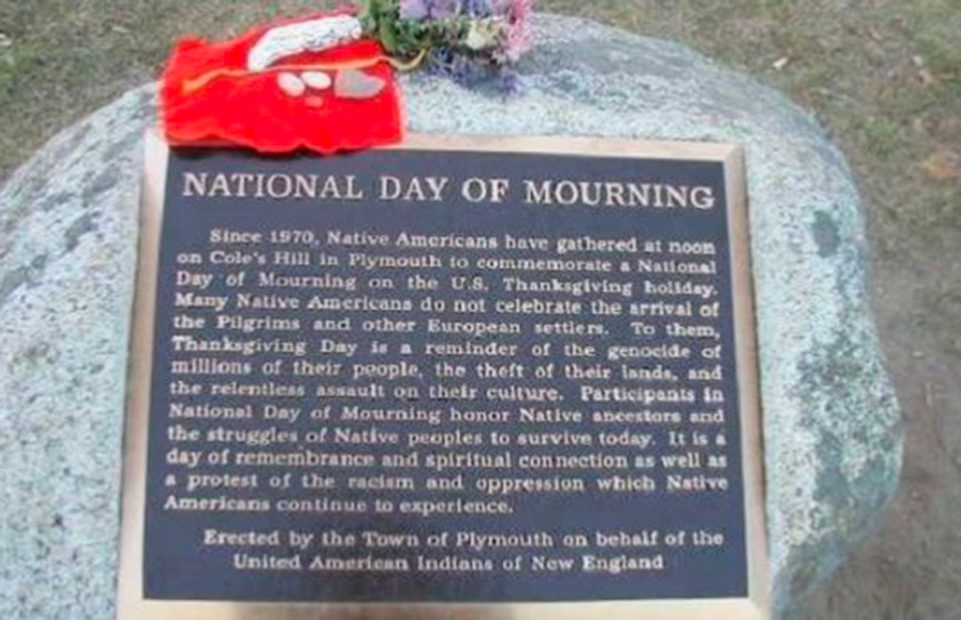 Plaque in Plymouth reading,"National Day of Mourning Since 1970, Native Americans have gathered at noon on Cole's Hill in Plymouth to commemorate a National Day or Mourning on the U.S. Thanksgiving holiday. Many Native Americans do not celebrate the arrival of the Pilgrims and other European settlers. To them, Thanksgiving Day is a reminder of the genocide of millions of their people, the theft of their lands, and the relentless assault on their cultures. Participants in National Day of Mourning honor Native ancestors and the struggles of Native peoples to survive today. It is a day of remembrance and spiritual connection as well as a protest of the racism and oppression which Native Americans continue to experience. Erected by the Town of Plymouth on behalf of the United American Indians of New England"