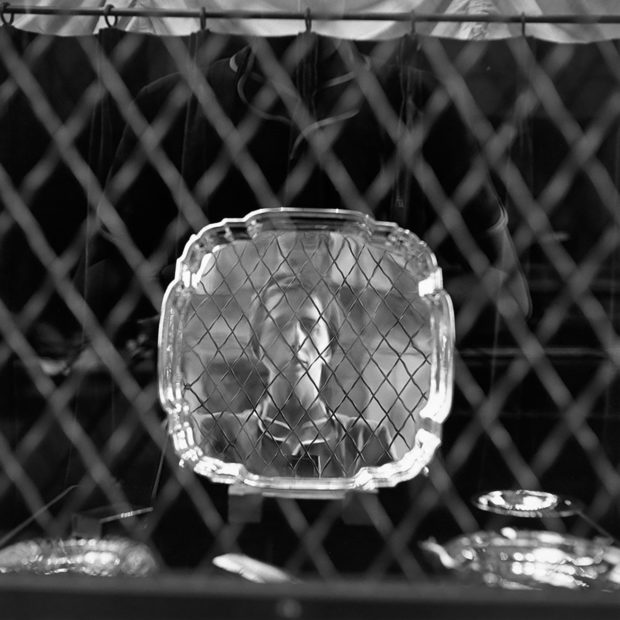 Vivian Maier reflected in a metal tray, displayed in a shop window.