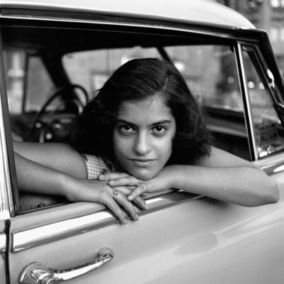 A girl looking out of a car window directly at the camera.