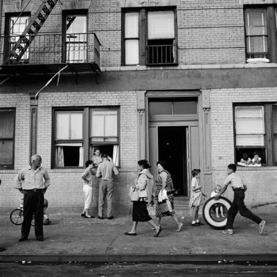 Various people outside a residential building, including a boy rolling a tyre