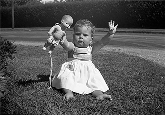 A baby girl holding out a doll and looking upset