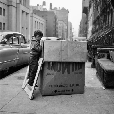 A boy looking into a box that is taller than him in the street