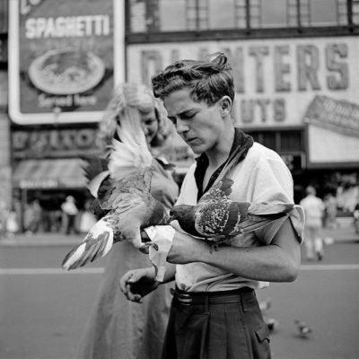 A man feeding pigeons that are on his hands, and a woman looking over his shoulder