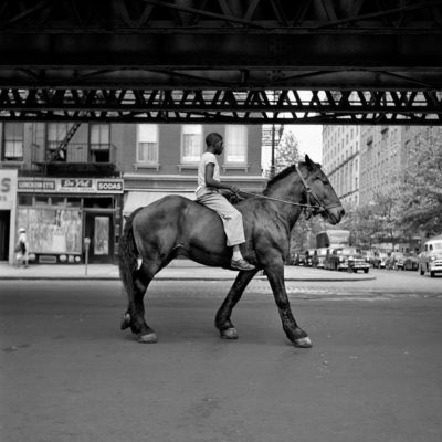 An Afrcian-American man riding a hose in the New York Streets,, under railway tracks.
