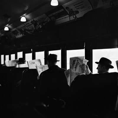 Several men in a train dressed identically and reading the newspaper