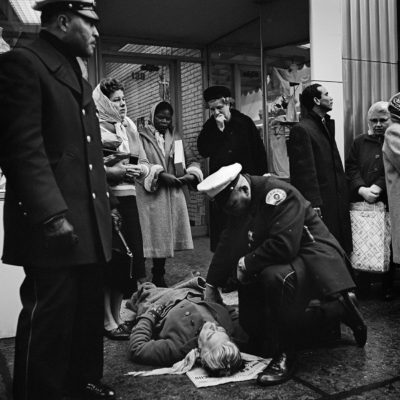 An injured person on the ground surrounded by police and a crowd