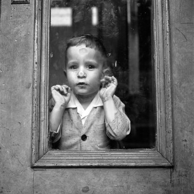 A little boy looking out through the glass pane of a door
