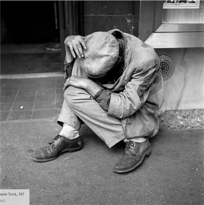 A man who looks uncared for, in a curled up position outside a building.