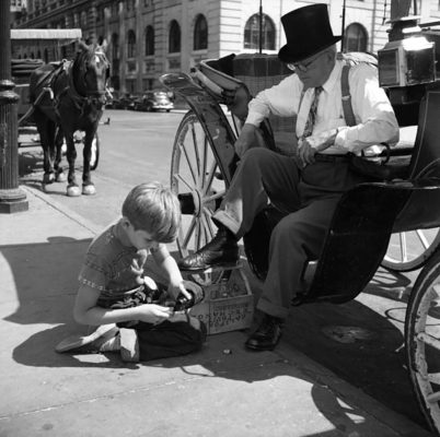 A young boy shining th e shoes of a Central Park carriage driver
