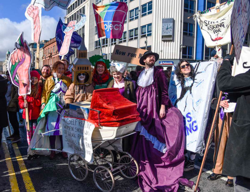 The collective in bright costumes with banners and slogans.