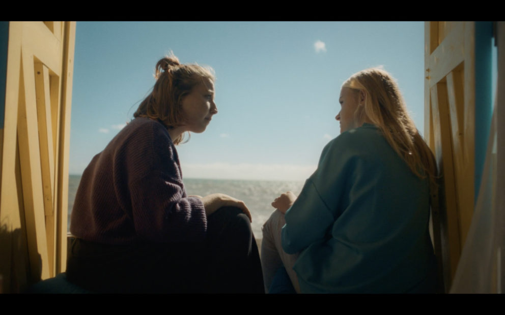 Two sisters sitting in a beach hut talking.