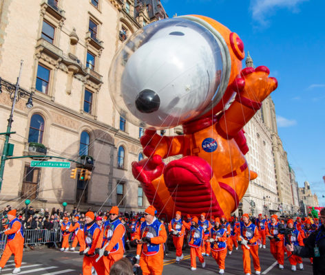 A Snoopy balloon in a NASA astronaut uniform, accompanied by people wearing a similar uniform.