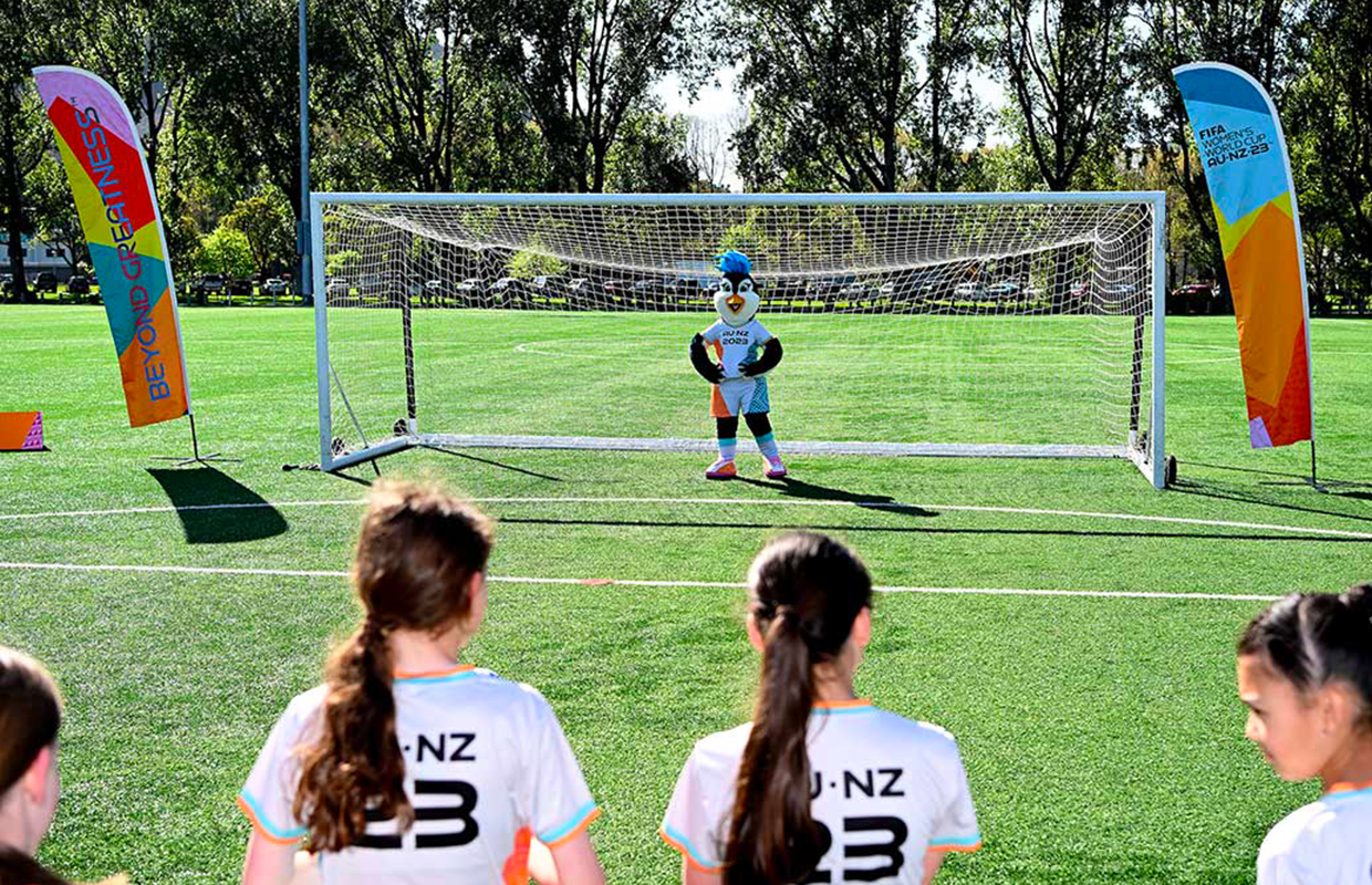 Girl football players facing Tazuni the mascot who is in goal.