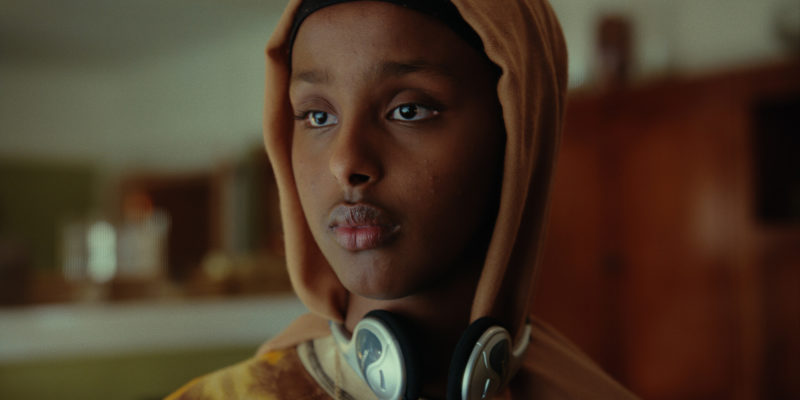 A still from the film Muna with the British-Somali title character wearing a hoodie and headphones.