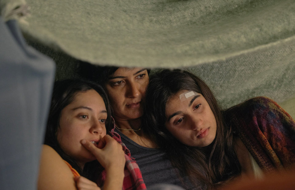 Two teenage girls and a woman, huddled together looking at something.