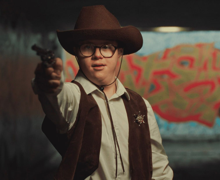 A still from the film Dusty Do Good showing a boy with Down's syndrome, dressed as a cowboy costume, pointing a toy gun at the camera.