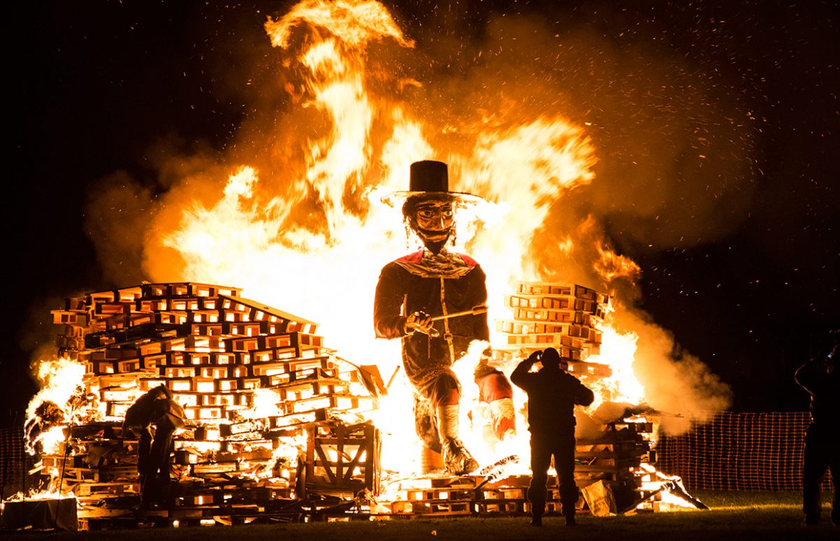 a person watching a Guy Fawkes model burn on a bonfire.
