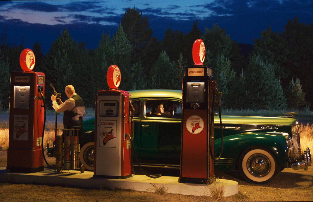 A photo reproduction of a Hopper painting of a green car getting petrol at a gas station at night