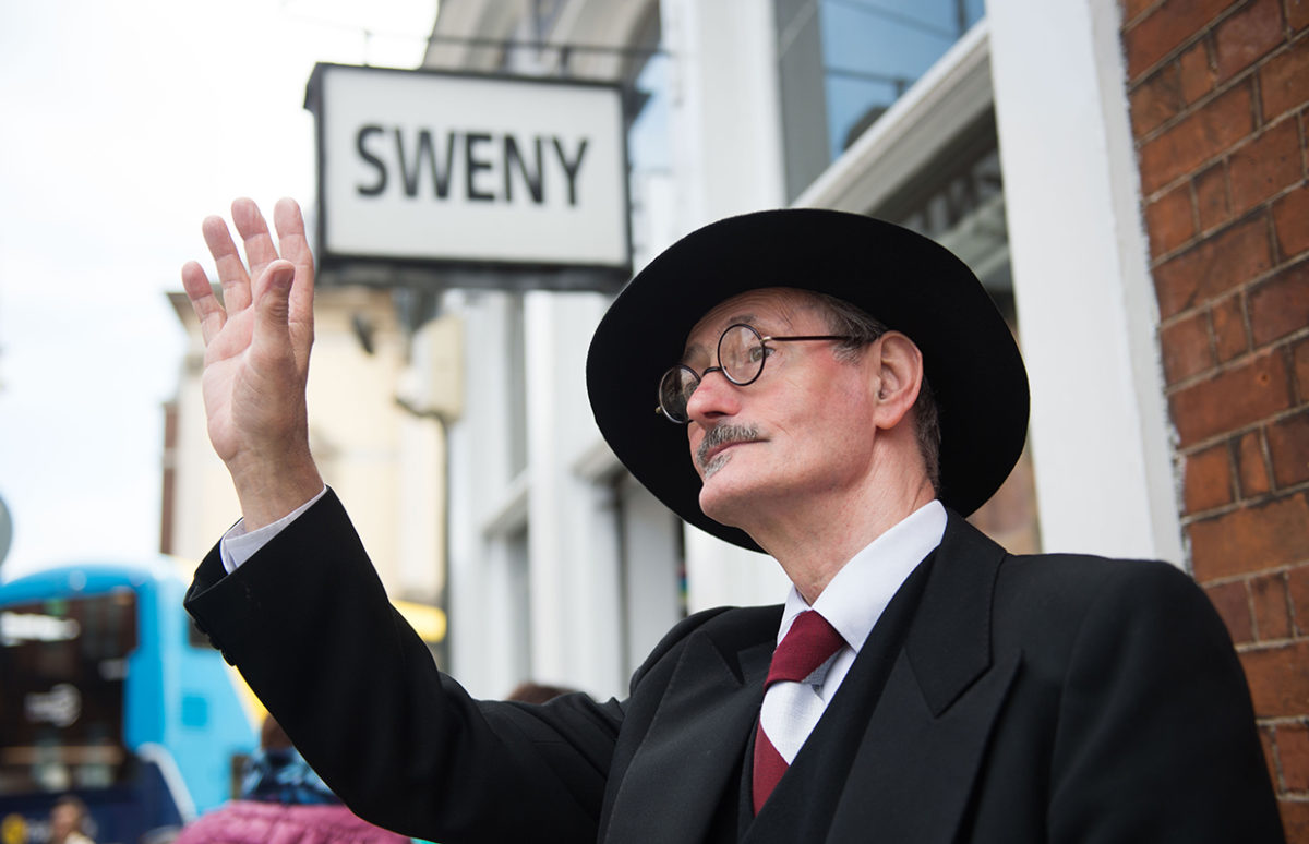 An actor dressed as James Joyce for Bloomsday, waving