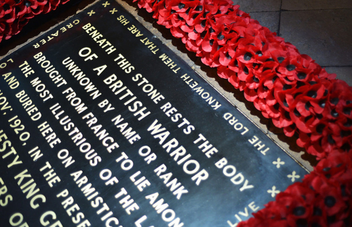 The tombstone of the Unknown Warrior in Westminster Abbey surrounded by red poppies for Remembrance Day. It reads: BENEATH THIS STONE RESTS THE BODY OF A BRITISH WARRIOR UNKNOWN BY NAME OR RANK BROUGHT FROM FRANCE TO LIE AMONG THE MOST ILLUSTRIOUS OF THE LAND