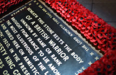 The tombstone of the Unknown Warrior in Westminster Abbey surrounded by red poppies for Remembrance Day. It reads: BENEATH THIS STONE RESTS THE BODY OF A BRITISH WARRIOR UNKNOWN BY NAME OR RANK BROUGHT FROM FRANCE TO LIE AMONG THE MOST ILLUSTRIOUS OF THE LAND