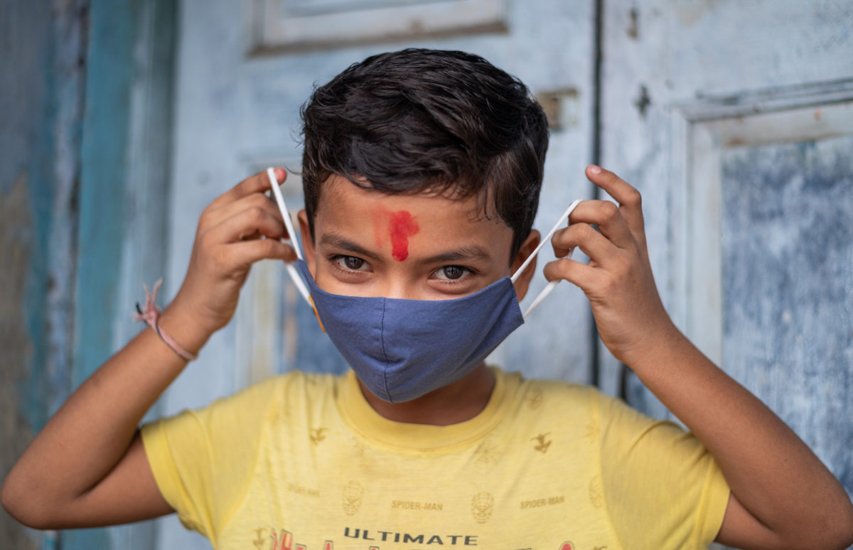 A young Indian boy putting on a facemask.