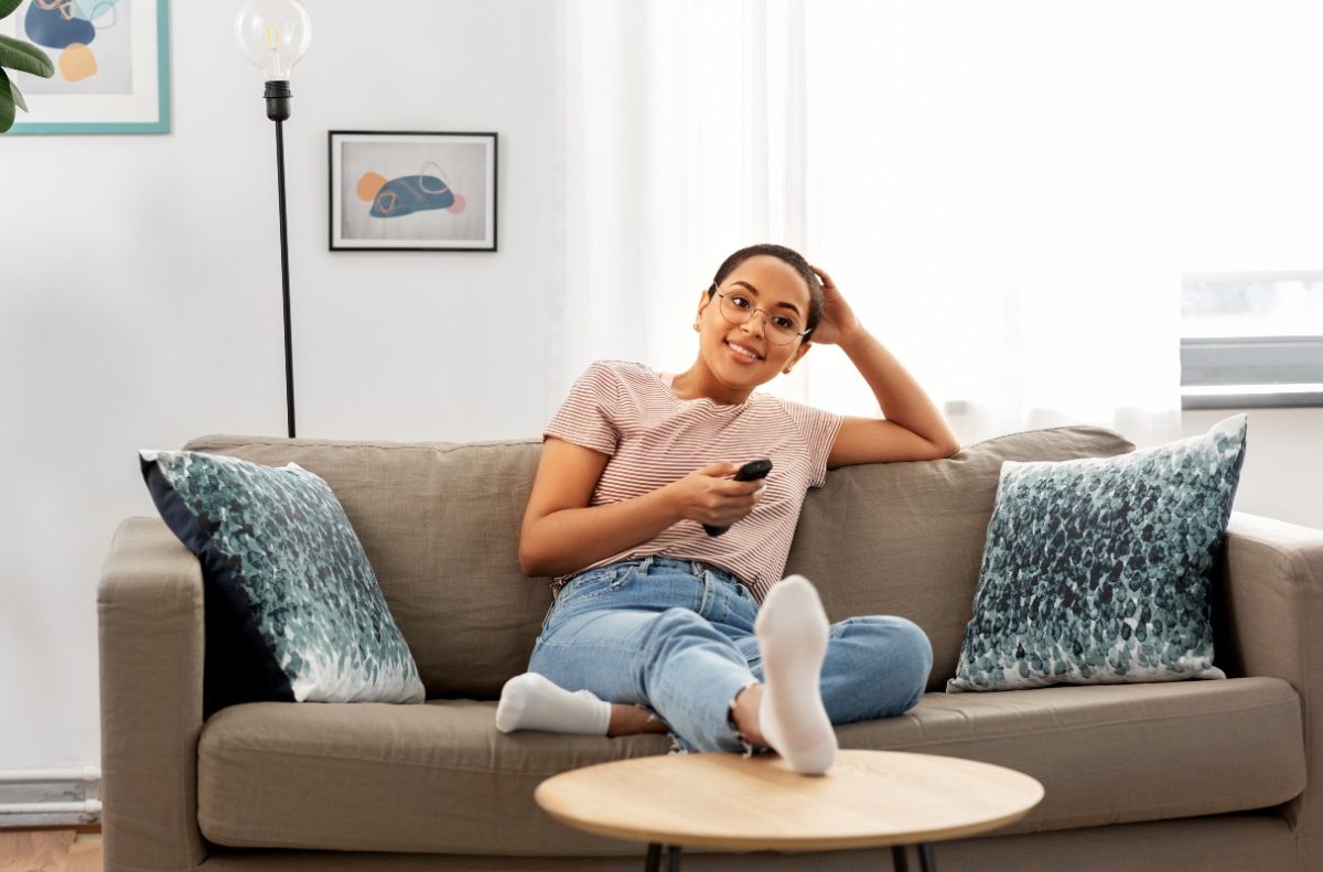 A woman sitting ona sofa with a TV remote control, apparently watching TV.