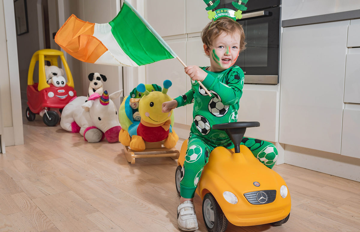 A young boy in green pyjamas holding an Irish flag leads a parade of his toys for St Patrick's Day.