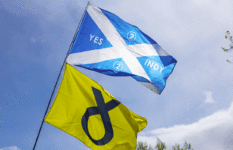 A Scottish flag reading "Yes Indy 2" and an SNP party flag at a pro-independence demonstration in Glasgow, 2019.