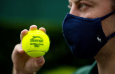 Amasked ball boy holding a ball marked Wimbledon 2021.