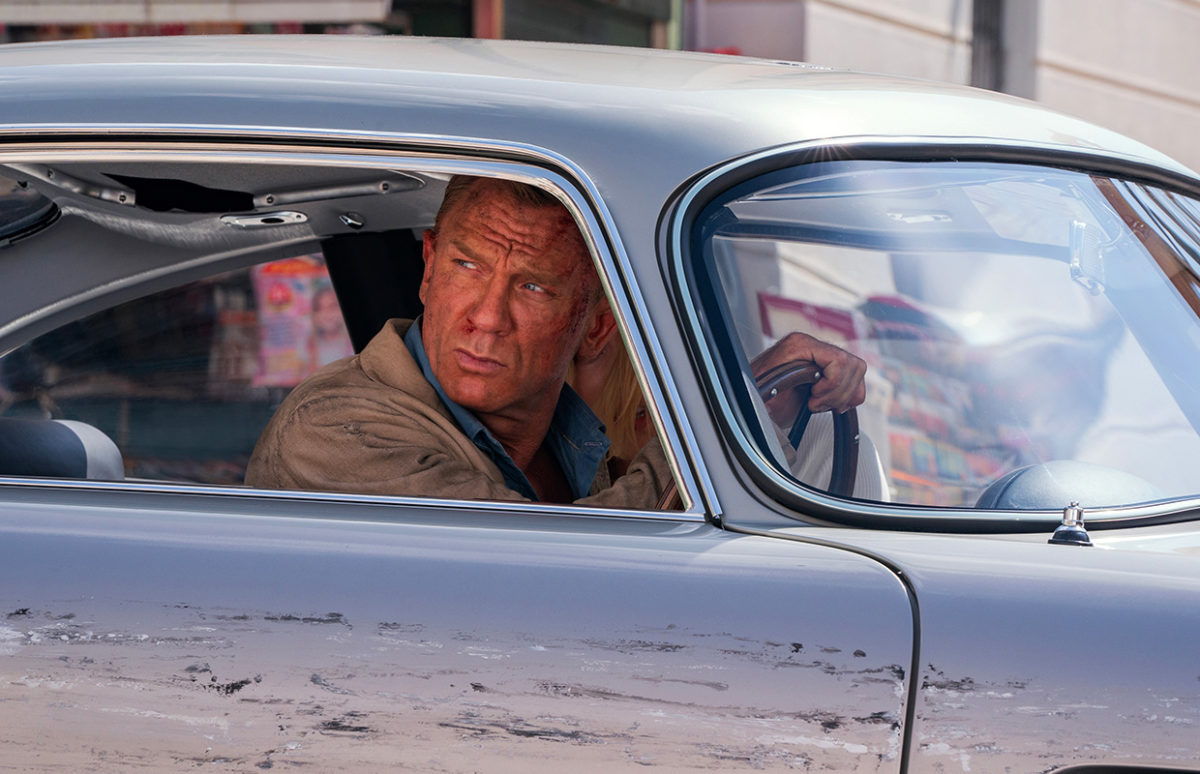 Daniel Craig as James Bond in a scratched car, in "No Time to Die".