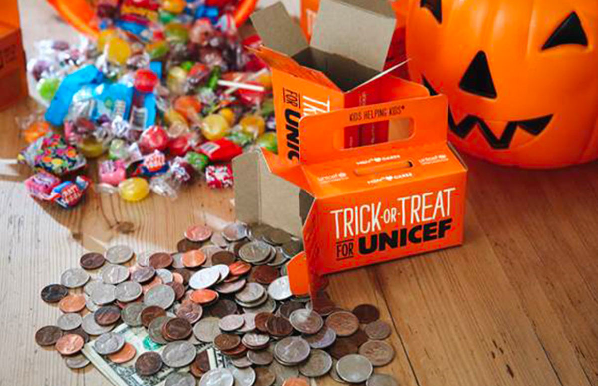 A Trick or treat for UNICEF collecting box surrounded by candy and a plastic jack o' lantern.