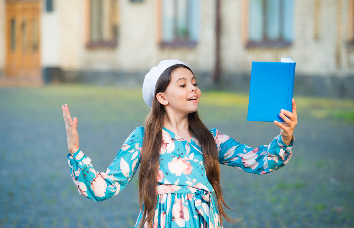 A teenager girl erciting from a book in the open air