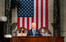 President Joe Biden addressing the Joint Houses of Congress in front of a U.S. flag and Kamala Harris and Nancy Pelosi (masked)