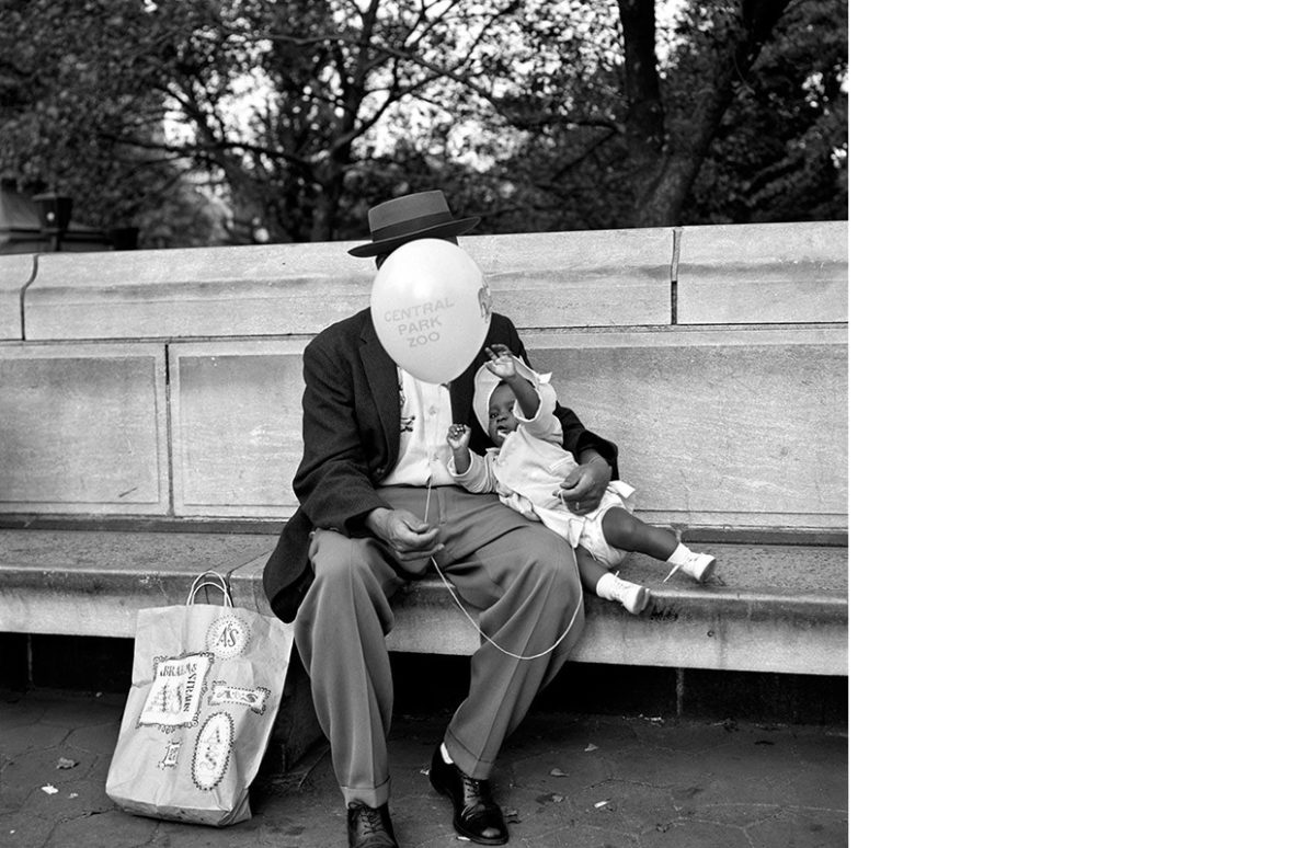 A man sitting on a park bench with a baby. A balloon hides his face.