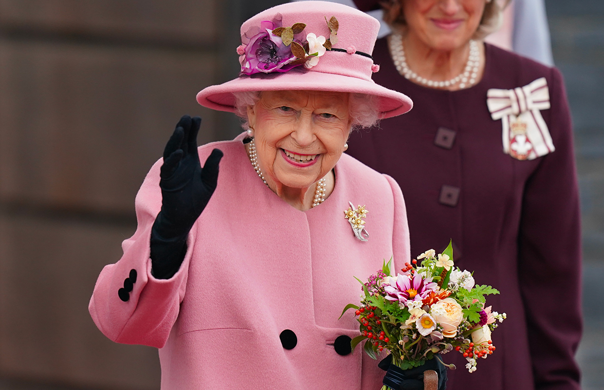 Queen Elizabeth II dressed in pink, waving and smiling.