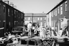 Buddy standing on top of a burnt out car, and other people participating in a barricade.