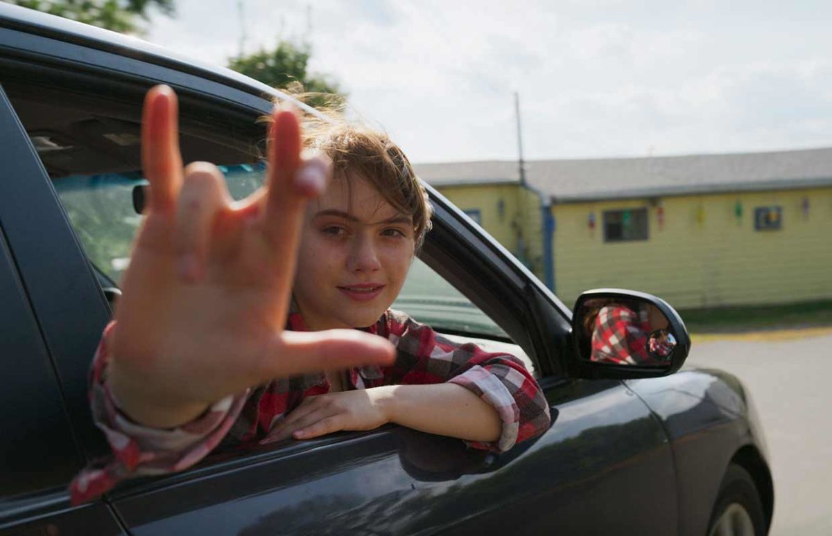 Emilia Jones as Ruby, signing "I love you" in using American Sign Language as she leans out of a car window in CODA.