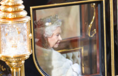 Queen ElizabethII in the state coach, wearing a crown.