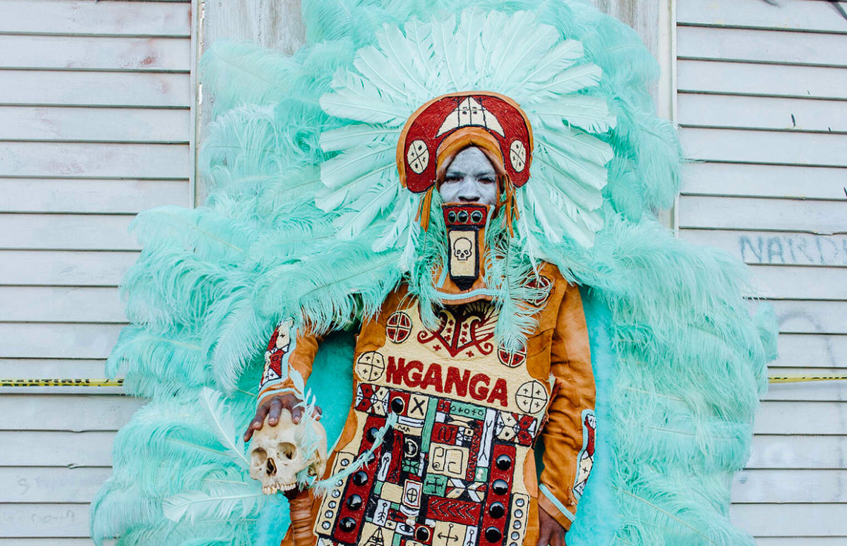 A man in an extravagant Mardi Gras costume with lots of feathers and holding a skull