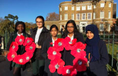 British schoolgirls in uniform holding wreaths of handmade poppies for Remembrance Day.
