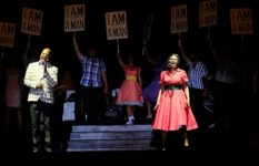Singers on a stage dressed in 1950s fashions, some of them holding signs saying I Am A Man from Martin Luther King's campaign.