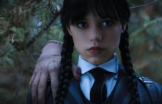 Jenna Ortega as Wednesday Addams, in school uniform, with a disembodied hand ("Thing") on her shoulder.