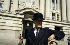 Bill Nighy as Williams in Living, looking at his watch outside London County Buildings, where he works