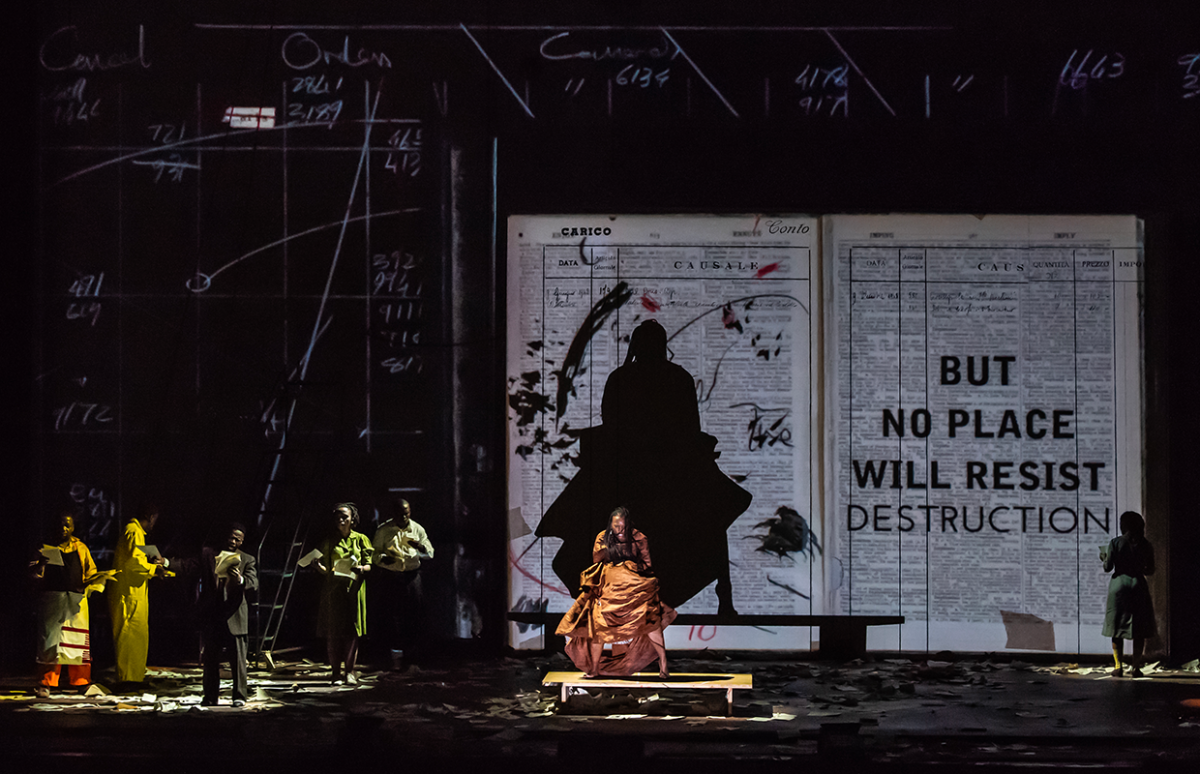 Dancers and musicians in front of a backdrop which reads No Place Will Resist Destruction